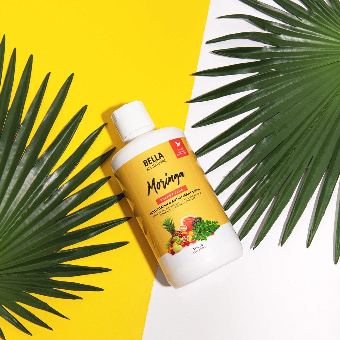 Jugo de Moringa Bella All Natural rodeado de hojas verdes