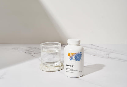 Botella de multivitamínico THORNE en escena minimalista junto a un vaso de agua.