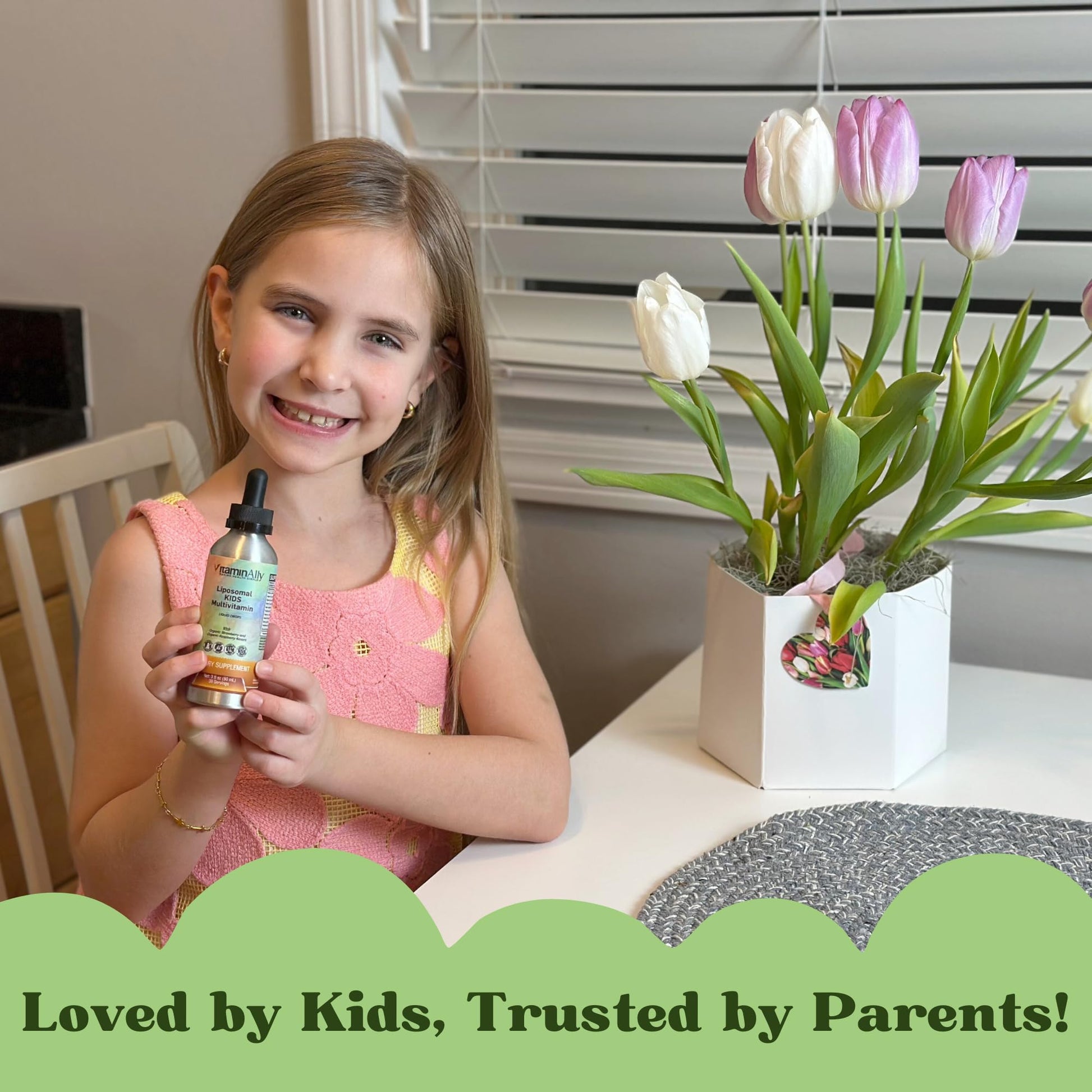 Niño sonriente sosteniendo multivitamínico Liposomal Kids junto a flores.