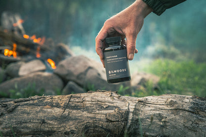 Persona sostiene multivitamínico To The Woods frente a un entorno natural.